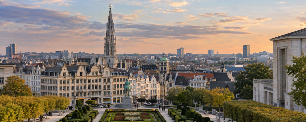 Brussels city centre skyline viewed from Mont des Arts, with the Gothic Brussels Town Hall spire rising above historic buildings at sunset.